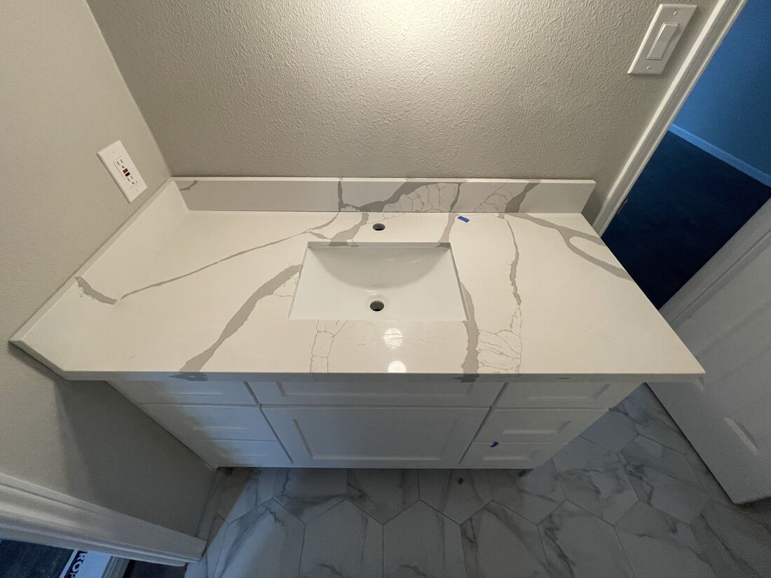 Single vanity top in white quartz with gray veining and a matching backsplash
